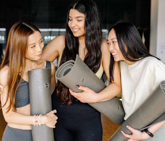 Three women holding yoga mats and hugging each other.