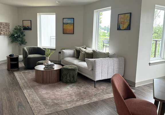 A living room with a white couch, a green chair, and a brown ottoman.