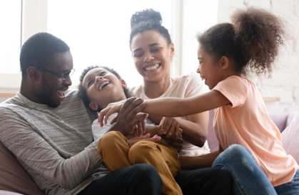 a family of four sitting on a couch laughing and holding their daughters hands