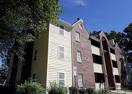 A building with a yellow siding and a brick section with a white sign on it.