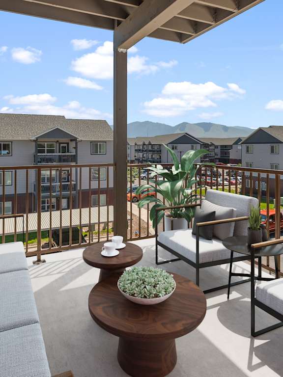 A balcony with a grey couch, a coffee table and a potted plant.