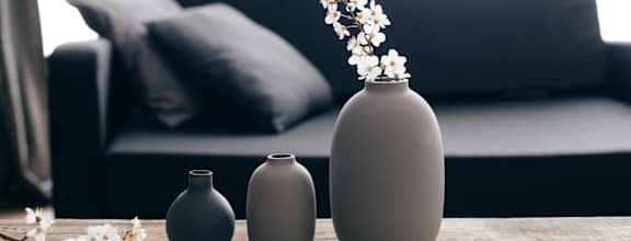 Three vases of different sizes are lined up on a table with a couch in the background.