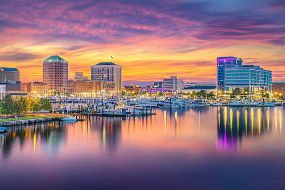 A city skyline at dusk with buildings reflecting in the water.