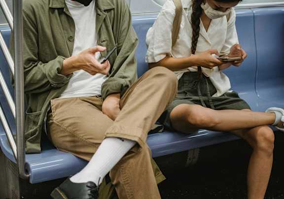 Two people sitting on a subway, both looking at their phones.