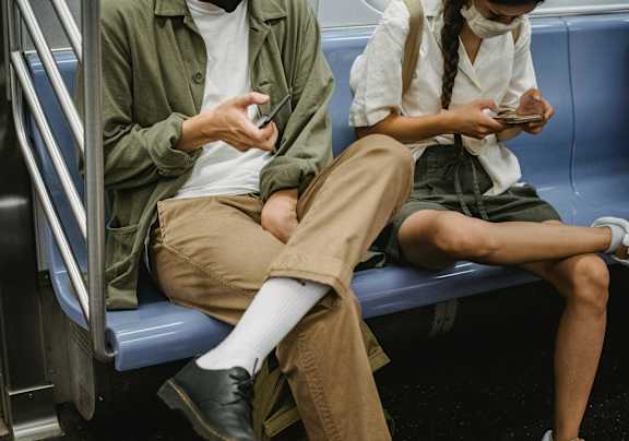 Two people sitting on a subway, both looking at their phones.
