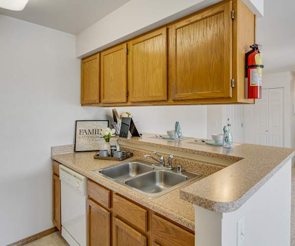 A kitchen with white appliances, light counter, and spacious wooden cabinets at La Maisonette Apartment Homes. 