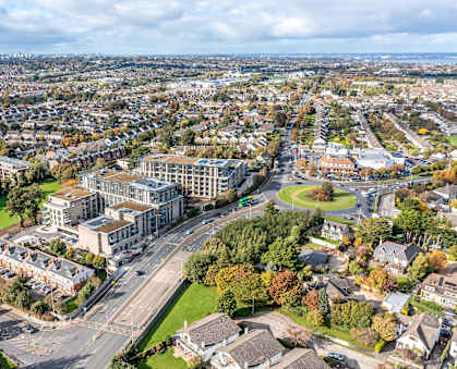 A cityscape with a mix of residential and commercial buildings, surrounded by trees with autumn foliage.