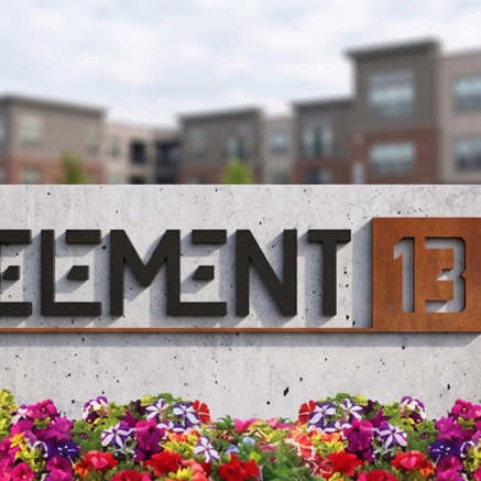 A sign that says Element 13 with flowers in front.
