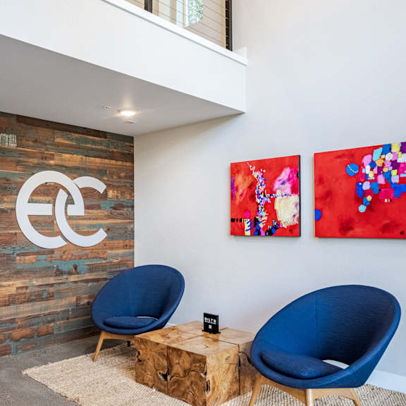 Two blue chairs are in front of a wooden wall with a Coca-Cola logo on it.