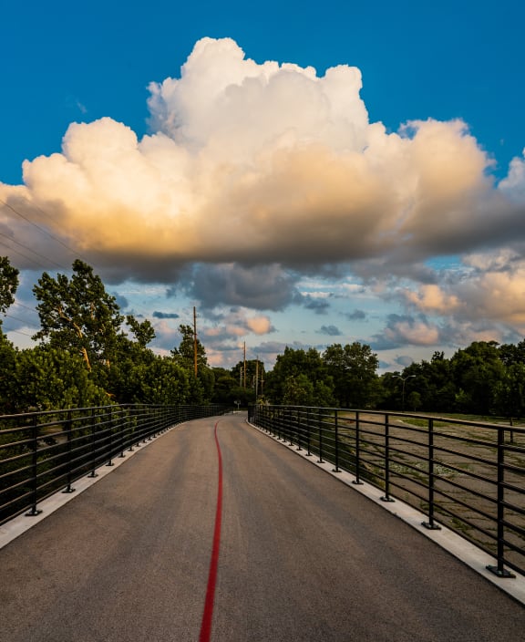 a road with a bridge and clouds in the sky
