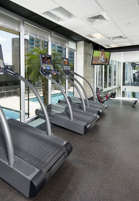 a room filled with cardio equipment and a large window with a pool in the background