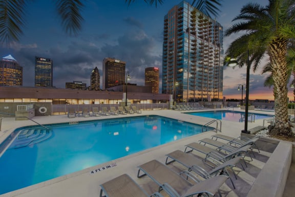 A pool with lounge chairs and palm trees in the foreground with a city skyline in the background. at Element, Tampa, FL, 33602