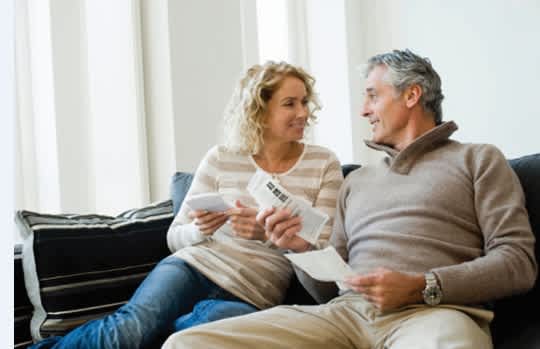 A man and a woman are sitting on a couch, both looking at a piece of paper.