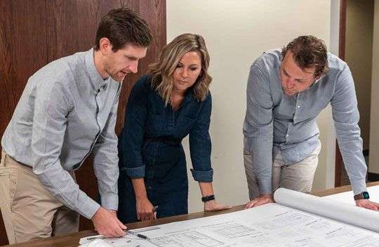 three people standing around a table looking at a blueprint