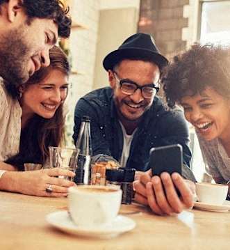 A group of people are sitting around a table with a cup of coffee and a smartphone.