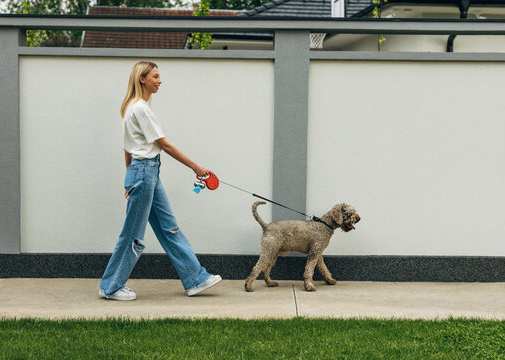 A woman walking her dog on a gravel path surrounded by trees.