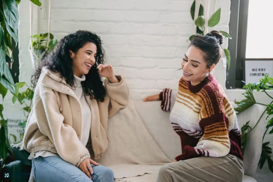 Two women sitting on a couch, one pointing at the other.