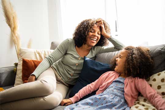 A woman and a young girl are sitting on a couch, laughing together.