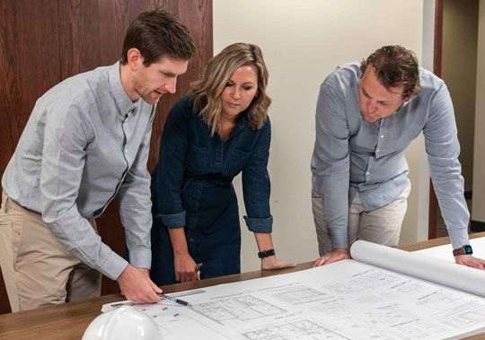three people standing around a table looking at a blueprint