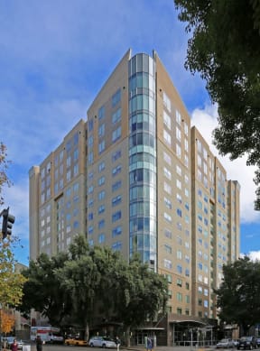 Apartments Downtown Sacramento - Building Exterior With a Column of Windows Spanning Up a Corner, Clear Sky, and Trees Surrounding the Building