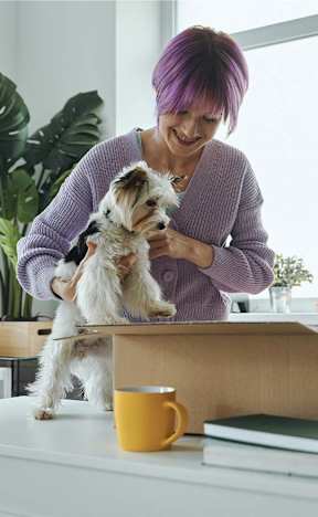 A woman with purple hair holds a small white dog.