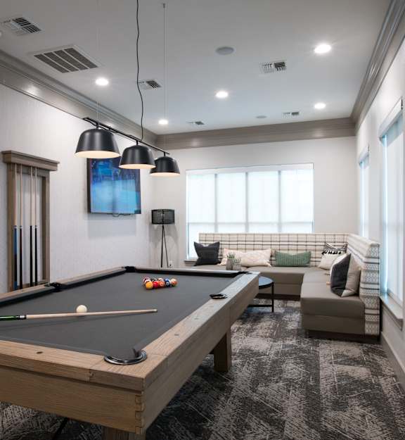 A pool table is in the middle of a room with a couch and a TV.