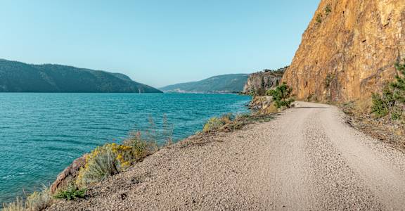 A dirt road leads down to a body of water with a cliff on the side.