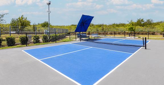 A blue tennis court with a white line in the middle and a black fence surrounding it.
