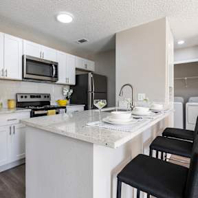 A kitchen with a white countertop and black chairs.