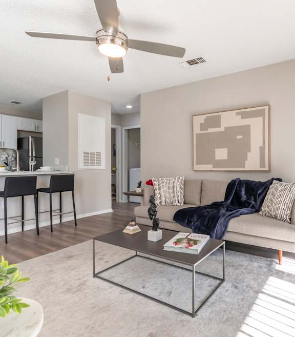 A modern living room with a grey sofa, a glass coffee table, and a ceiling fan.