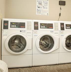 Three identical front loading washing machines are lined up in a laundromat.