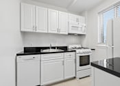 Thumbnail 24 of 59 - A white kitchen with black countertops and white appliances.