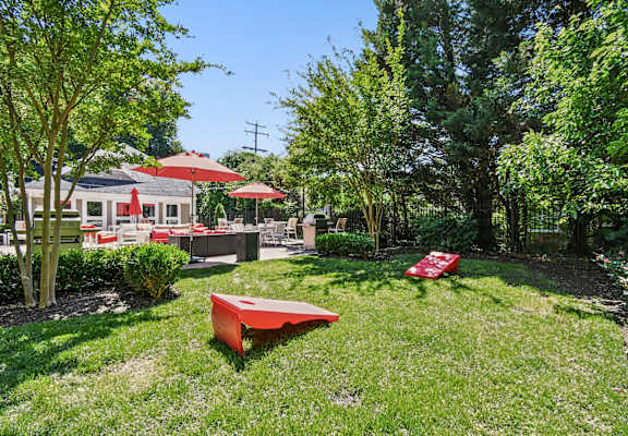 A red bench sits in a grassy area with trees and a building in the background.