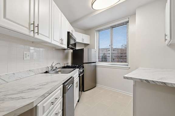 A kitchen with white cabinets, stainless steel appliances, and a marble countertop.