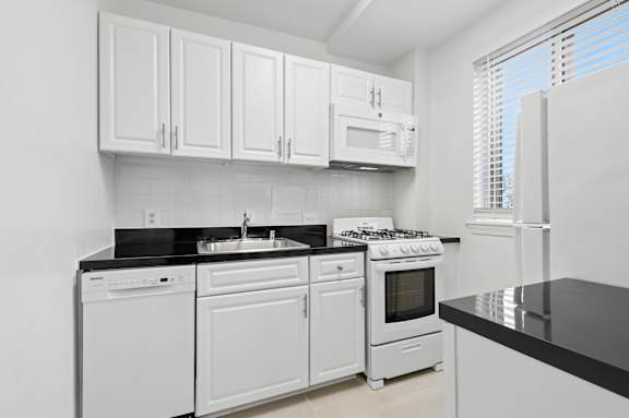 A white kitchen with black countertops and white appliances.