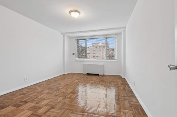 A room with wooden flooring and a window overlooking a building.