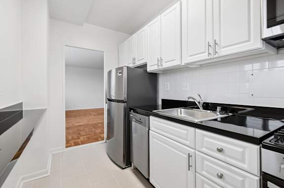 One bedroom kitchen with white cabinets, stainless steel appliances, and black countertops.