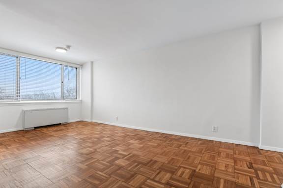 A room with a wooden floor and a window with blinds.
