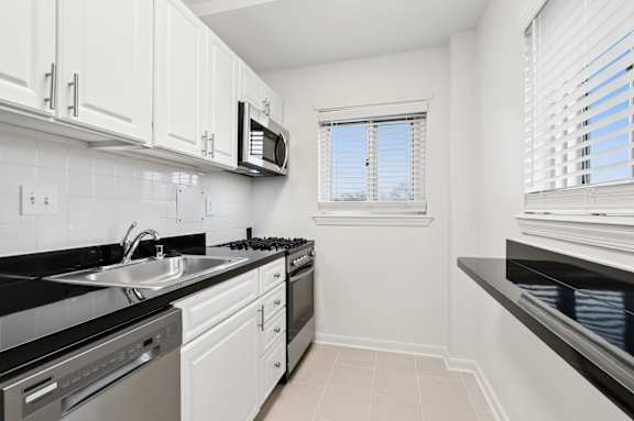 A kitchen with white cabinets and black countertops.
