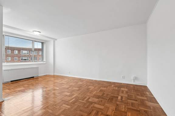A room with wooden flooring and a window overlooking a building.