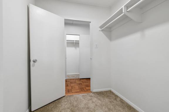 A white door opens to a hallway with a carpeted floor.