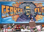 a woman holding a sign in front of a wall with a mural and flowers