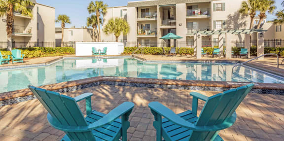 a swimming pool with blue chairs around it in front of an apartment building