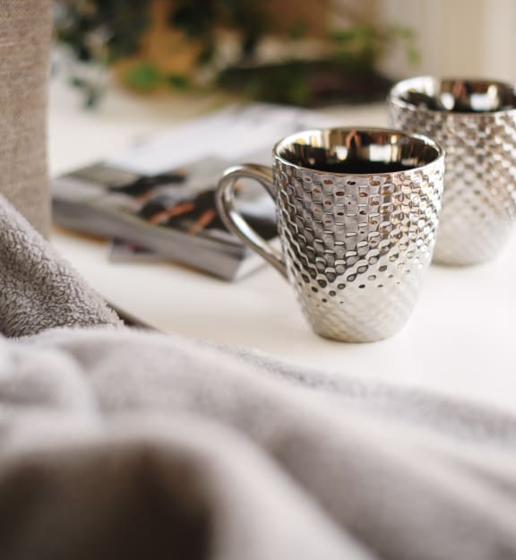 two cups on a table next to a bed with a blanket
