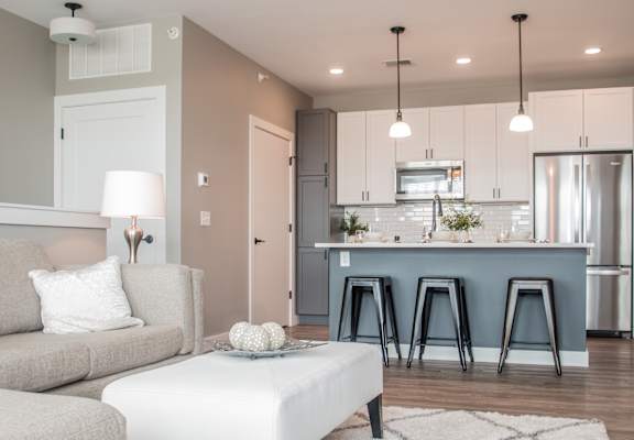 A modern living room with a grey couch, a white coffee table, and a kitchen area in the background.