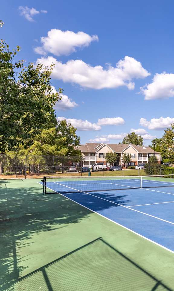 A tennis court surrounded by trees and a building in the background.