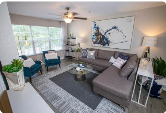A living room with a grey couch, a blue chair, a coffee table, and a ceiling fan.