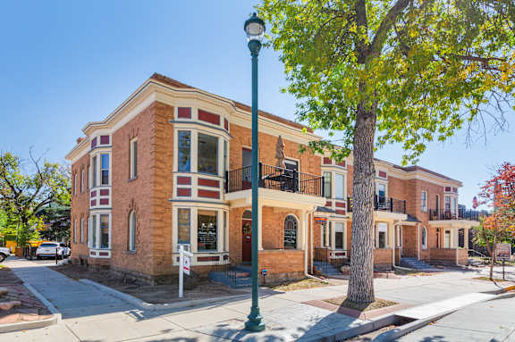 A street view of a two-story brick building with a tree in front.