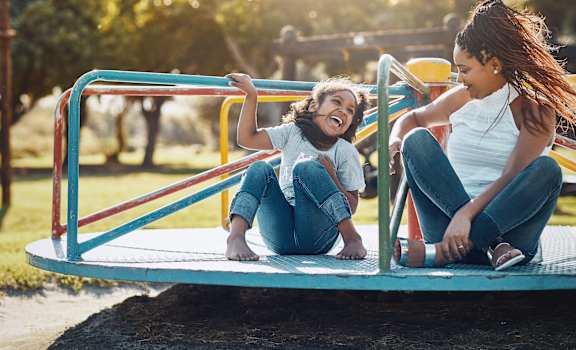 a mother and daughter playing on a playground merry go round