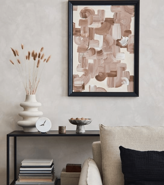 A living room with a couch, a shelf with books and a vase, and a framed artwork on the wall.